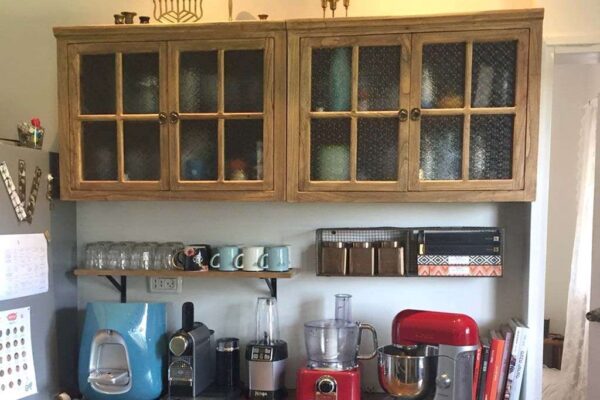 מטבח מעוצב עם ארון עץ, מכשירי חשמל, כוסות ומדפים לקופסאות, משדר אווירה נוחה.