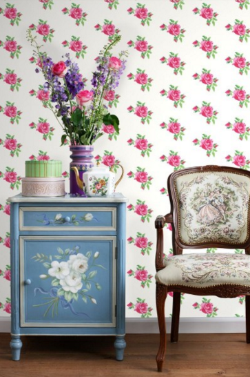 שולחן צד מעוצב עם פרחים, כוסות וקישוטים, מול טפט פרחוני וכיסאות מעוצבים.