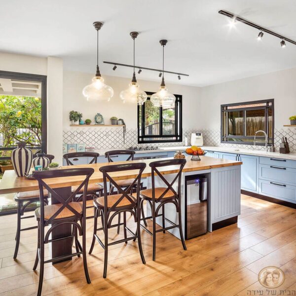 מטבח מעוצב עם שולחן אוכל וספסלים, גופי תאורה תלויים, חלון פתוח ופינת ישיבה נעימה.