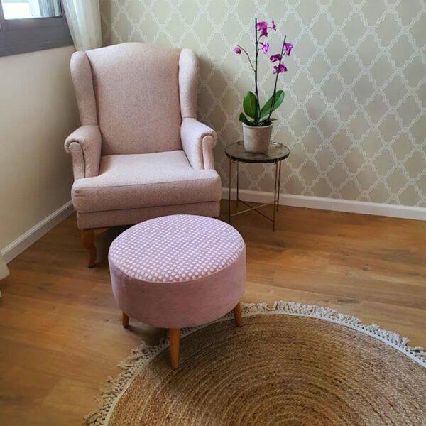 כורסה מעוצבת בצבע ורוד ושולחן קטן עם פרח, שטיח עגול מעוצב ורקע עם טפטים לקיר.